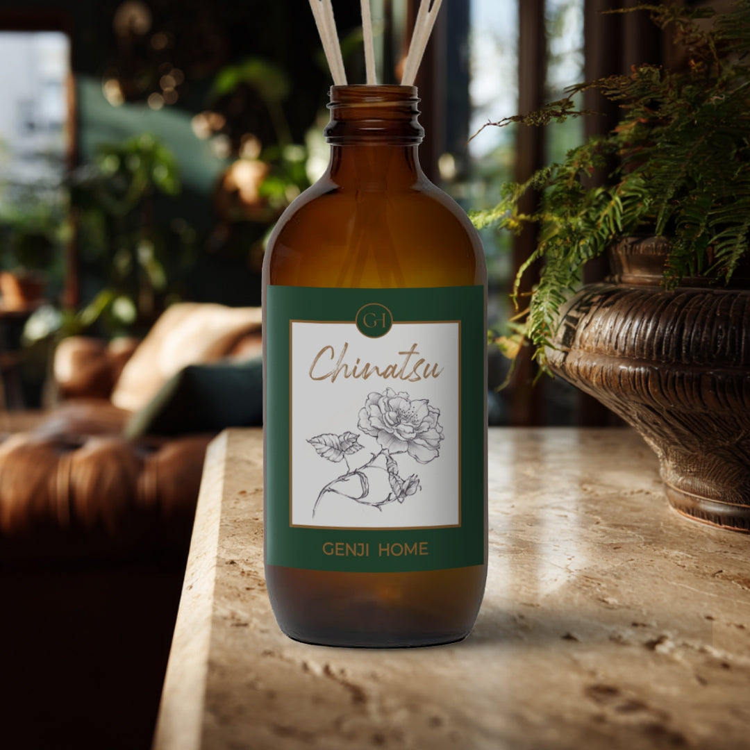 Chinatsu Reed Diffuser by Genji Home in an amber bottle on a travertine surface with a blurred natural background of plants and decor.