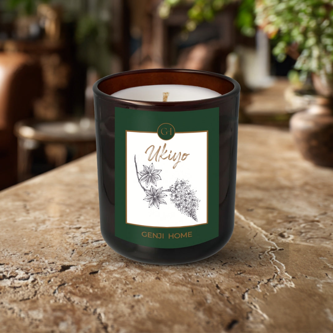 Ukiyo Olive Wax Candle by Genji Home in an amber bottle on a travertine surface with a blurred natural background of plants and decor.