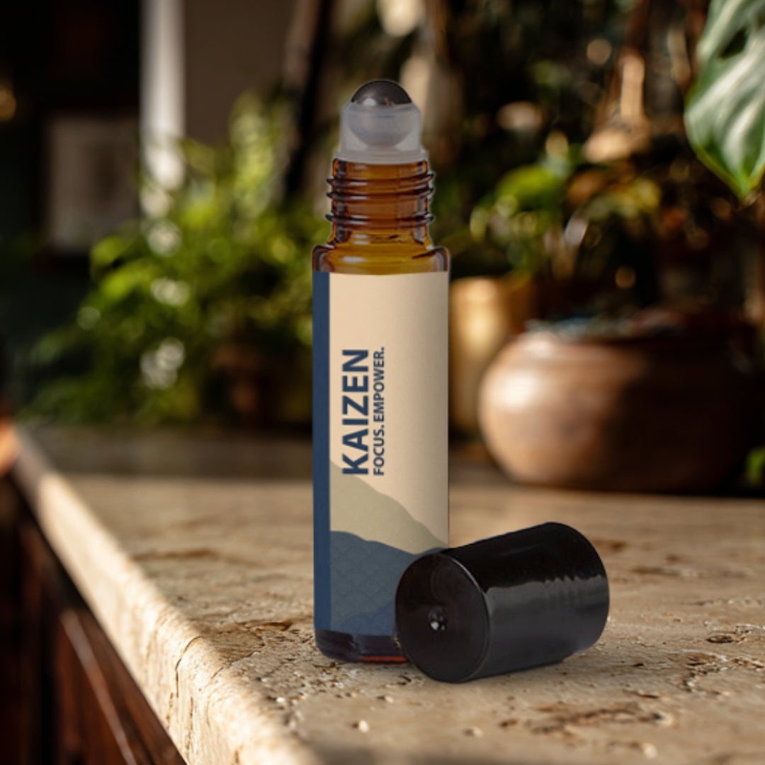 Kaizen essential oil roller bottle on a travertine surface with plants in the background.