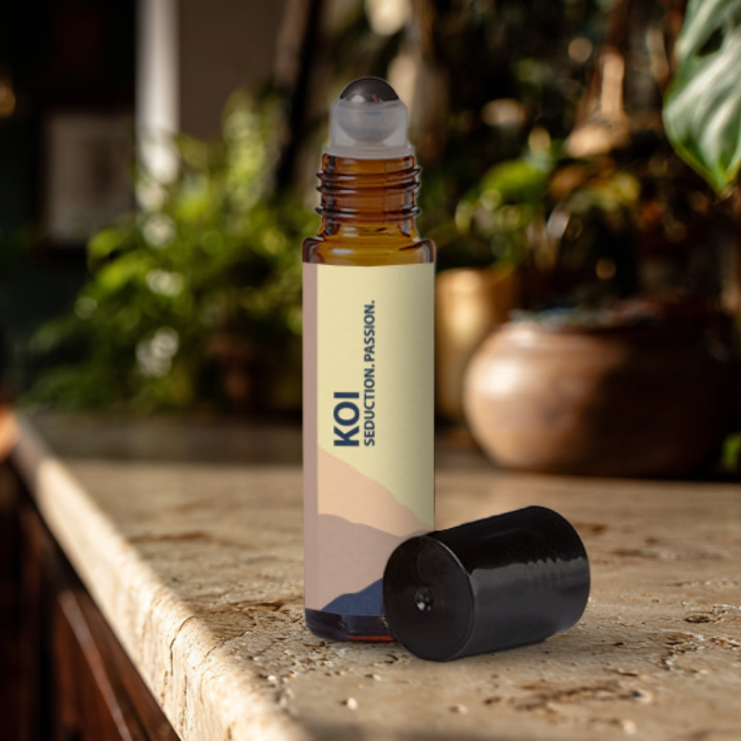 Koi essential oil roller bottle on a travertine surface with plants in the background.