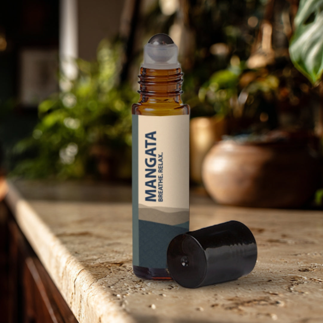 Mangata essential oil roller bottle on a travertine surface with plants in the background.