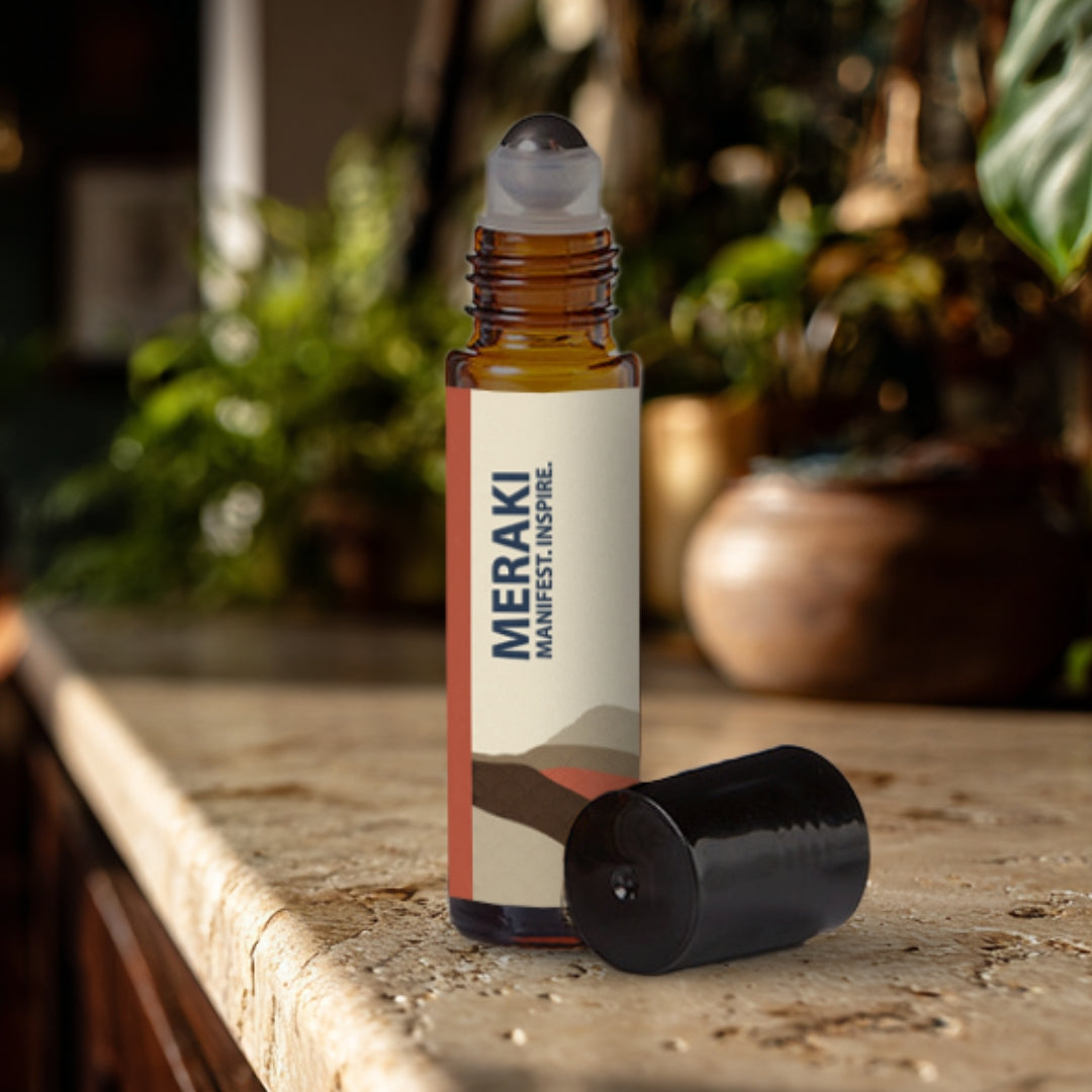 Meraki essential oil roller bottle on a travertine surface with plants in the background.