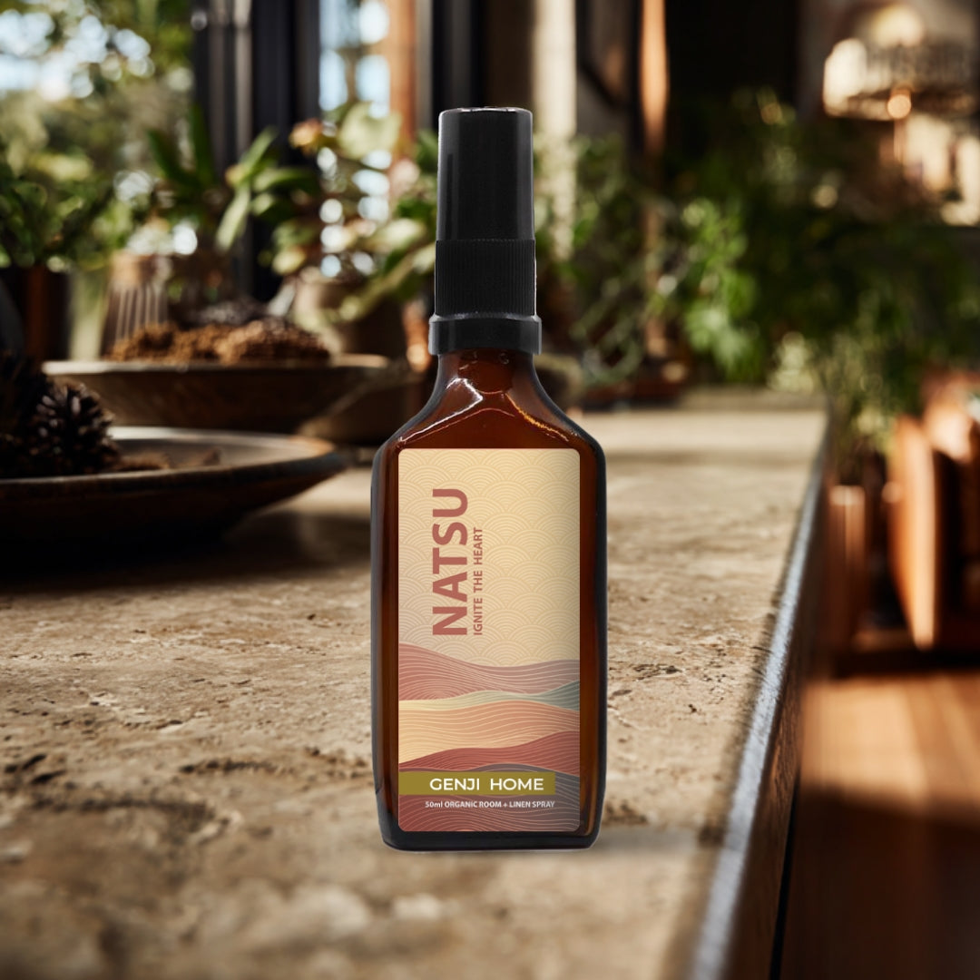 Natsu room and linen spray by Genji Home in an amber bottle on a travertine surface with a blurred natural background of plants and decor.