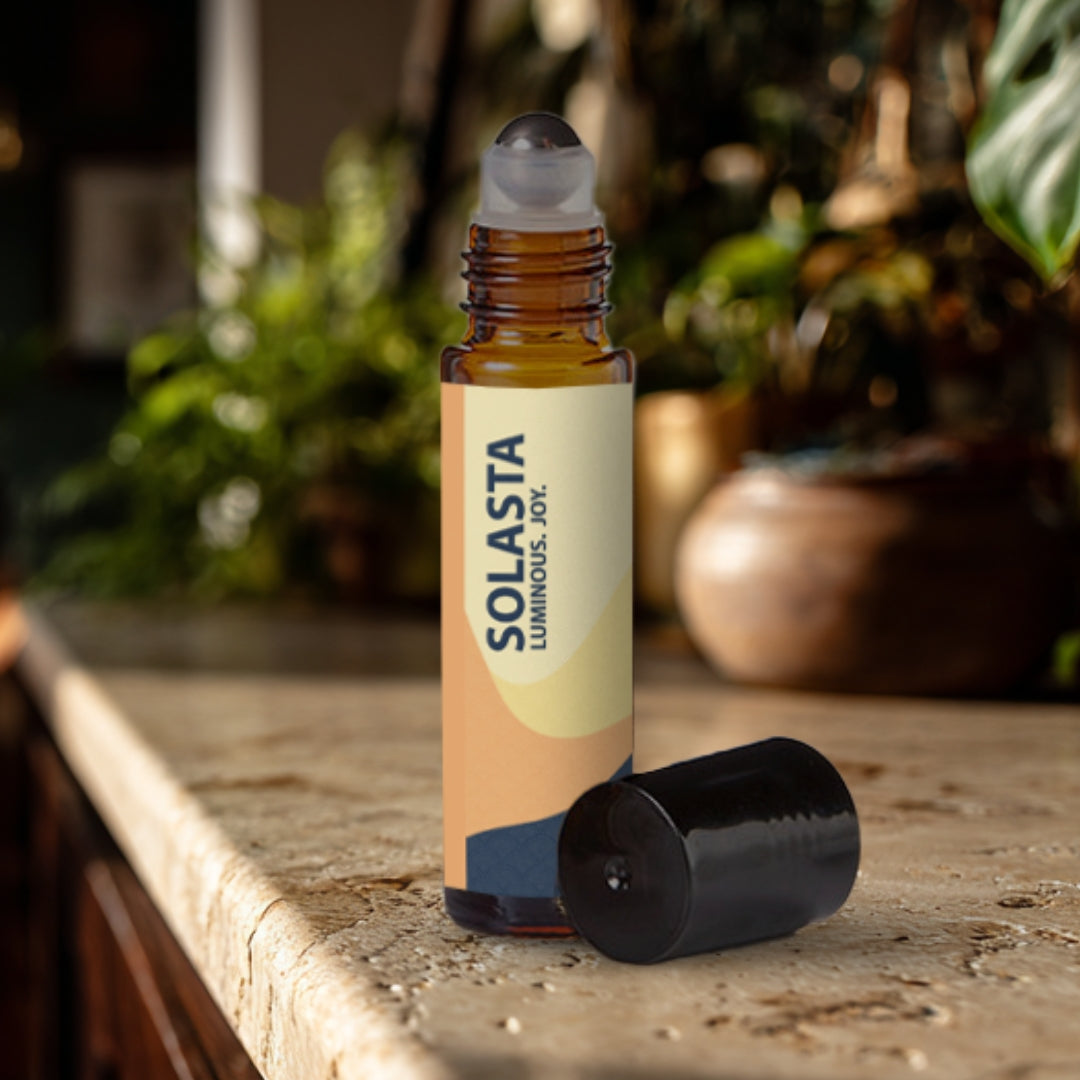 Solasta essential oil roller bottle on a travertine surface with plants in the background.