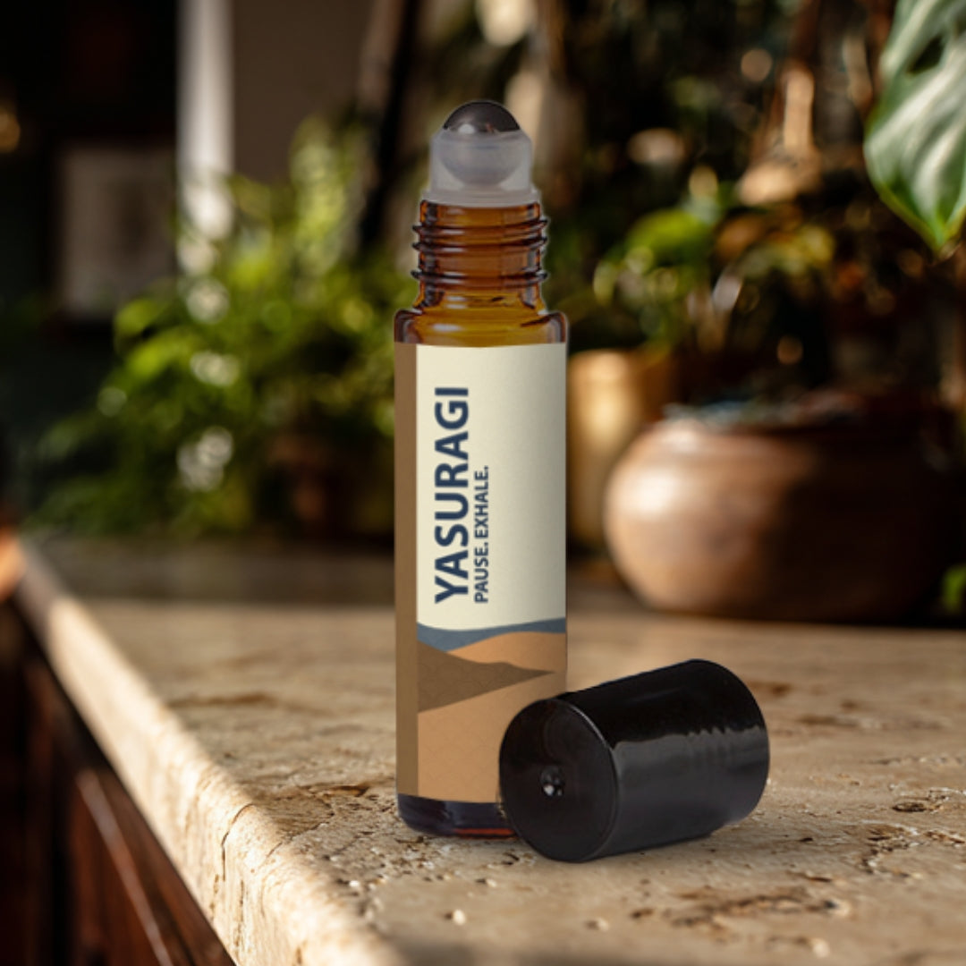 Yasuragi essential oil roller bottle on a travertine surface with plants in the background.