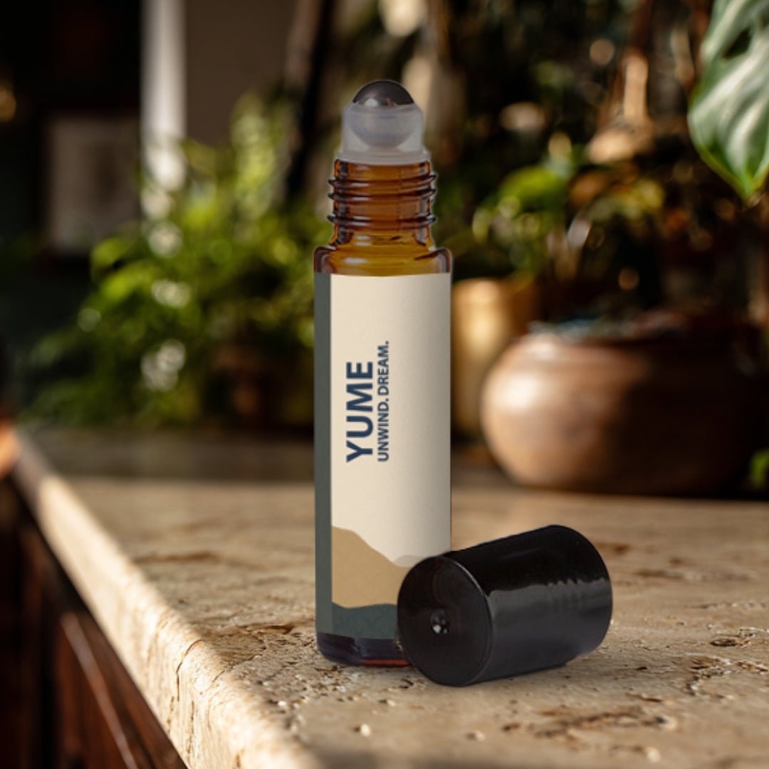Yume essential oil roller bottle on a travertine surface with plants in the background.