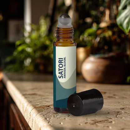 Satori essential oil roller bottle on a travertine surface with plants in the background.