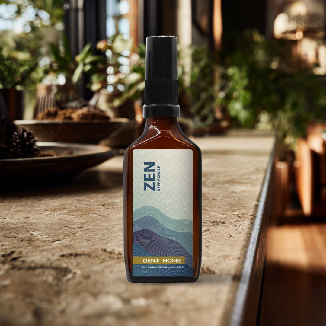 Zen room and linen spray by Genji Home in an amber bottle on a travertine surface with a blurred natural background of plants and decor.